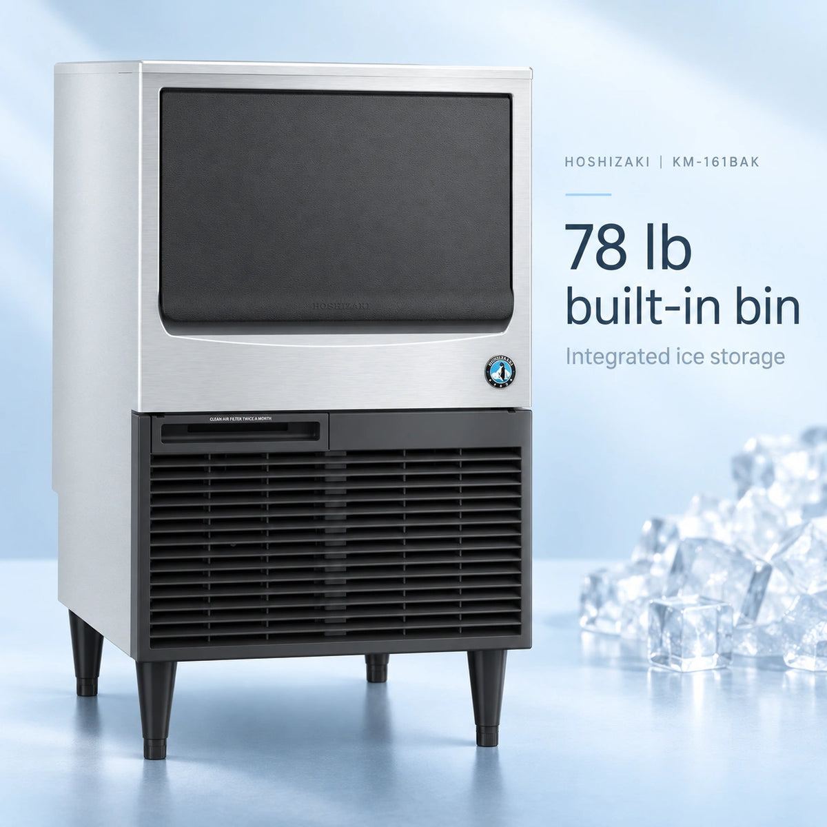 A Hoshizaki KM-181BAK commercial ice machine with a brushed silver upper cabinet and black lower cabinet, featuring a built-in 78 lb ice storage bin. The machine is shown on a reflective light blue studio floor with a pile of clear ice cubes on the right and text overlay detailing its features.