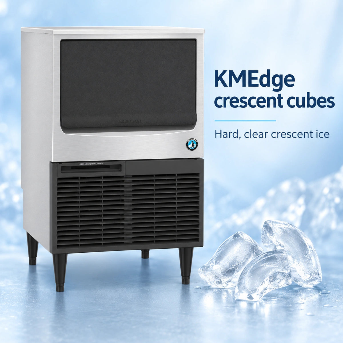 A commercial ice machine with a brushed silver metal front and black lower grille, shown on a icy blue background with text reading 'KMEdge crescent cubes' and several clear ice cubes in the foreground.