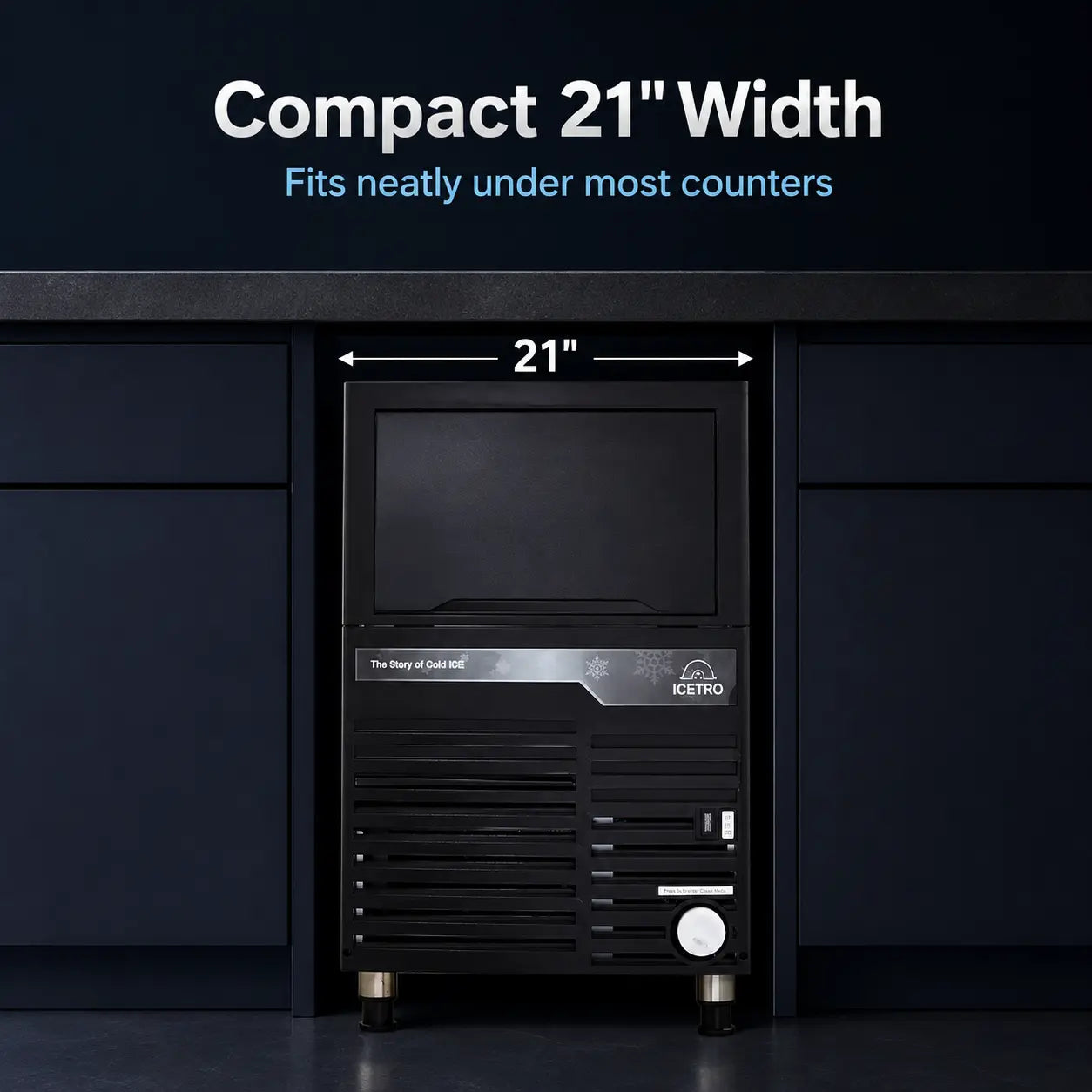 A compact black ice machine shown installed under a counter, with text overlays indicating a 21-inch width. The machine has a dark front panel with a silver accent strip and a white circular button near the bottom right.