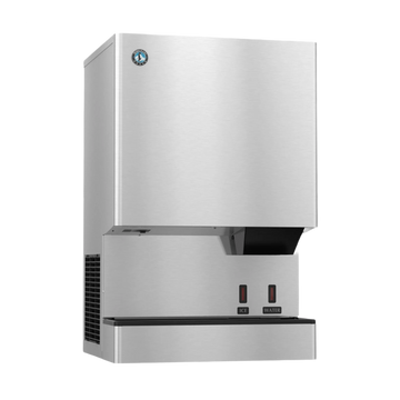 A stainless steel commercial ice machine with a brushed metal finish, featuring a black drip tray, two red power switches, and a small circular logo badge on the upper left front panel.